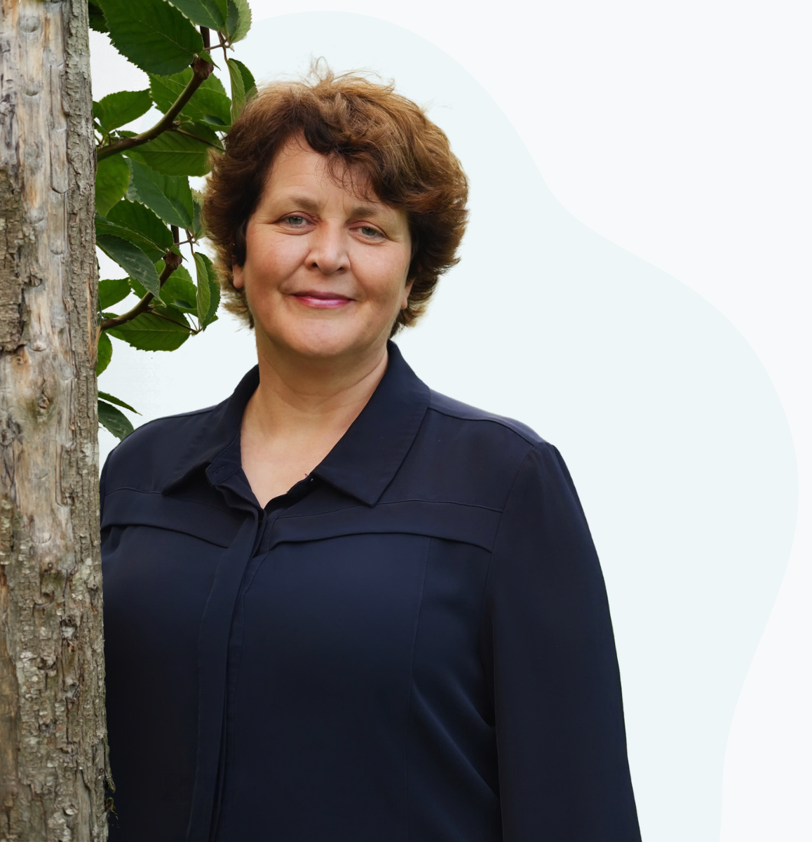 Nely Sieffers staat naast een boom, met een lichtblauwe organische vorm op de achtergrond.